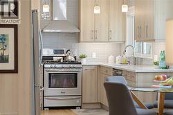 Contemporary kitchen featuring light wood-finish cabinetry, stainless steel appliances, a tile backsplash, and pendant lighting - 