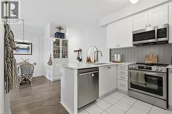 Kitchen featuring white shaker cabinetry, stainless steel appliances, a white tile floor, and a peninsula with a white countertop - 