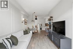 Open-concept living space with light wood-finish flooring, white walls featuring decorative wall molding, and recessed lighting - 