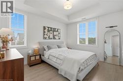 Bedroom featuring light wood-finish flooring, a tray ceiling, and two large windows with white blinds - 