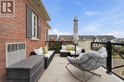 Spacious outdoor balcony featuring a concrete surface, a brick exterior wall, a white-framed window with dark shutters, and a black glass railing system - 