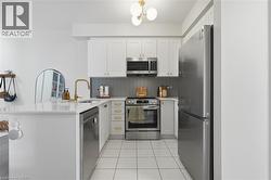 Modern kitchen featuring white cabinetry, stainless steel appliances, a white quartz-finish countertop, a gold-finish faucet, and white tile flooring - 