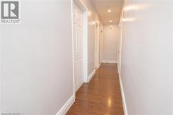 Hallway featuring wood-finish flooring, white baseboards, recessed lighting, and multiple paneled doors - 