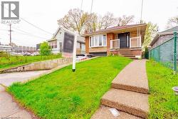 Brick exterior featuring a bay window, concrete front walk with steps, a covered porch with white railings, and a driveway leading to an integrated garage - 
