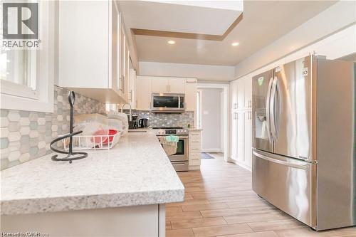 Contemporary kitchen featuring stainless steel appliances, light wood-finish flooring, white cabinetry, a hexagonal tile backsplash, and light-toned countertops - 574 Upper Sherman Avenue, Hamilton, ON 