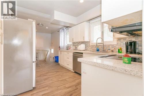 Kitchen featuring white cabinetry, light-toned countertops, tile backsplash, stainless steel appliances, and wood-finish flooring - 574 Upper Sherman Avenue, Hamilton, ON 
