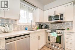 Modern kitchen featuring stainless steel appliances, white cabinetry, a patterned tile backsplash, and light-colored countertops - 