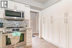 Modern kitchen featuring white shaker cabinetry with brushed nickel hardware, stainless steel appliances, a mosaic tile backsplash, and wood-finish flooring - 