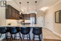 Kitchen featuring dark wood-finish cabinetry, stainless steel appliances, a light-toned countertop island with pendant lighting, and a subway tile backsplash - 
