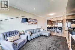 Open-concept living space featuring crown molding, hardwood-style flooring, a built-in electric fireplace, and a kitchen with stainless steel appliances, dark wood cabinetry, and pendant lighting - 