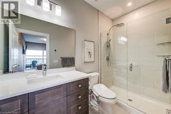 Contemporary bathroom featuring a spacious glass-enclosed shower with a rainfall showerhead, a single-sink vanity with a white countertop, dark wood-finish cabinetry, and a full-width mirror with heat - 