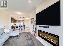 Open-concept living area featuring a wall-mounted electric fireplace, engineered wood flooring, crown molding, a kitchen island with pendant lighting, and stainless steel appliances - 