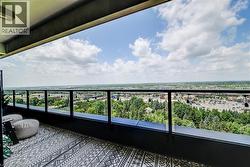 Expansive outdoor balcony featuring a glass and metal railing, geometric pattern flooring, and a broad cityscape backdrop - 