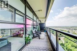 Expansive private balcony featuring a glass and metal railing, geometric pattern outdoor rug, and high-rise cityscape - 