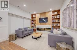 Living area featuring a contemporary linear fireplace with a stone surround, integrated wood-finish shelving, recessed lighting, and wood-finish flooring - 