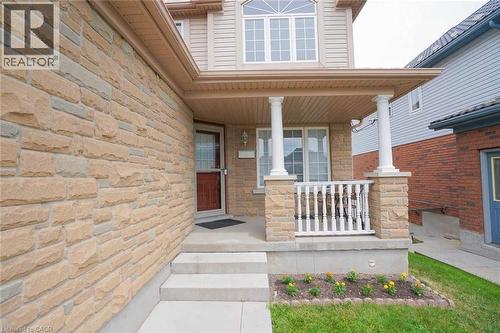 Stone facade residence featuring a covered front porch with decorative columns and railings, a main entry door with a screen door, concrete steps, and an upper-level bay window - 187 Adler Drive, Cambridge, ON - Outdoor