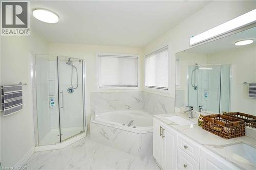 Spacious bathroom featuring a corner soaking tub with a tiled surround, a glass-enclosed shower, dual vanities with white cabinetry and integrated sinks, and contemporary white tile flooring - 187 Adler Drive, Cambridge, ON - Indoor Photo Showing Bathroom