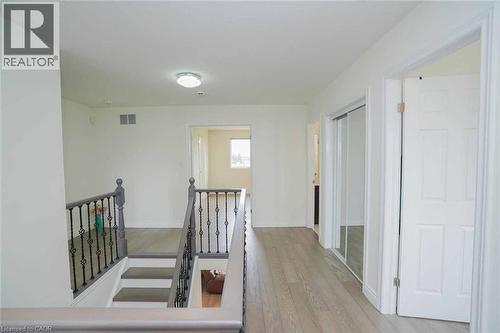 Upper-level landing featuring wood-finish flooring, white walls, a staircase with dark gray railings and decorative wrought iron spindles, a hallway with mirrored closet doors, and multiple doorways l - 187 Adler Drive, Cambridge, ON - Indoor Photo Showing Other Room