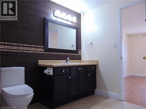 Bathroom featuring a dark tiled accent wall with a mosaic band, a black vanity with a light countertop, a framed mirror, and a modern toilet - 214 Snowdrop Crescent, Kitchener, ON 
