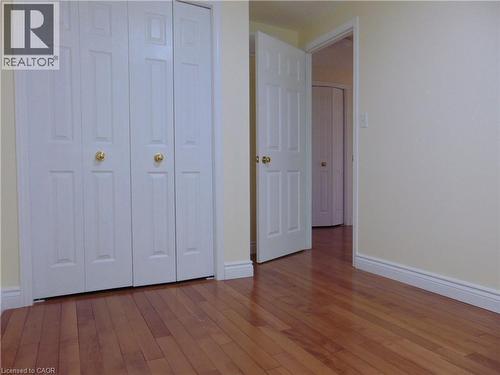 Room featuring wood-finish flooring, light-toned wall paint, white trim, and bi-fold closet doors with brass hardware - 214 Snowdrop Crescent, Kitchener, ON 