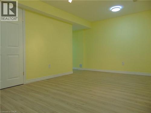 Spacious room with wood-finish flooring, light yellow walls, white baseboards, and a flush-mount ceiling light - 214 Snowdrop Crescent, Kitchener, ON 