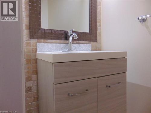 Contemporary vanity featuring light wood-finish cabinetry with polished chrome hardware, an integrated sink, and a matching backsplash - 214 Snowdrop Crescent, Kitchener, ON 