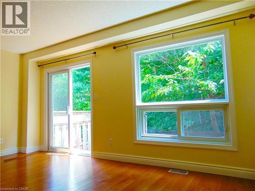 Sunlit interior with wood-finish flooring, a sliding glass door opening to an outdoor deck, and a large multi-pane window providing ample natural light - 214 Snowdrop Crescent, Kitchener, ON 