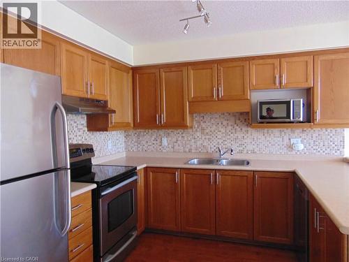 Kitchen featuring wood cabinetry, a mosaic tile backsplash, a double basin stainless steel sink, and stainless steel appliances - 214 Snowdrop Crescent, Kitchener, ON 
