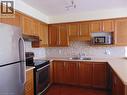 Kitchen featuring wood cabinetry, a mosaic tile backsplash, a double basin stainless steel sink, and stainless steel appliances - 214 Snowdrop Crescent, Kitchener, ON 