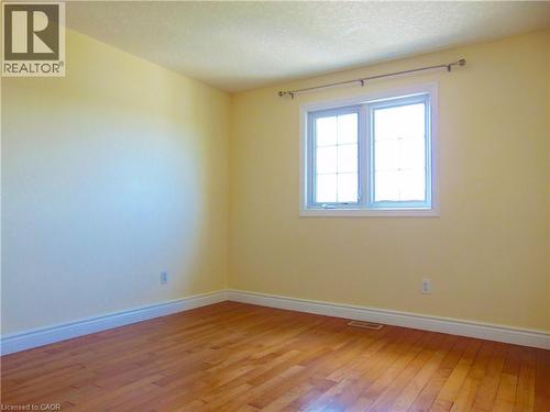 Bedroom featuring wood-finish flooring, light yellow painted walls, white baseboards, and a double-pane window with white trim - 214 Snowdrop Crescent, Kitchener, ON 