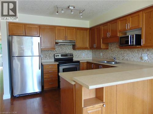 U-shaped kitchen featuring wood cabinetry, stainless steel appliances, mosaic tile backsplash, and light-toned countertops - 214 Snowdrop Crescent, Kitchener, ON 