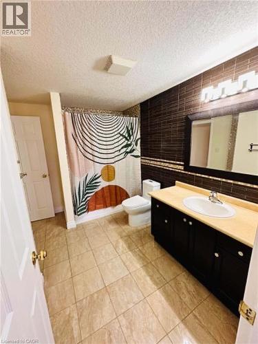 Bathroom featuring tiled flooring, a dark wood-finish vanity with an integrated sink, a full wall mirror, and a tiled shower surround - 214 Snowdrop Crescent, Kitchener, ON 
