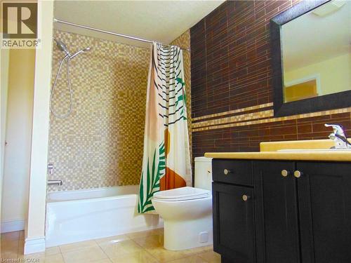 Bathroom featuring a white bathtub, mosaic-tiled shower surround, dark brown wall tiling with accent stripe, black vanity with a light-colored countertop, and a recessed sink - 214 Snowdrop Crescent, Kitchener, ON 