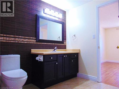 Bathroom featuring a dark subway tile accent wall with a decorative mosaic band, a black vanity with a light-colored countertop, and a rectangular framed mirror with vanity lighting - 214 Snowdrop Crescent, Kitchener, ON 
