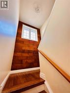 Staircase featuring wood-finish flooring, a coordinating wood accent wall, a white-framed window, and a contemporary ceiling light fixture - 