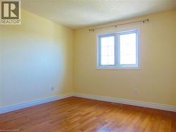 Bedroom featuring wood-finish flooring, light yellow painted walls, white baseboards, and a double-pane window with white trim - 