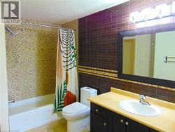 Bathroom featuring a built-in bathtub with mosaic tile surround, a dark wood-finish vanity with an integrated sink, a large wall-mounted mirror, and a modern light fixture - 