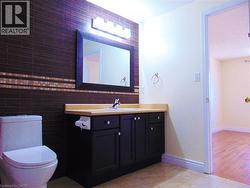Bathroom featuring a dark subway tile accent wall with a decorative mosaic band, a black vanity with a light-colored countertop, and a rectangular framed mirror with vanity lighting - 