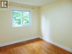 Bright interior space of bedroom featuring a dual-pane window, wood-finish flooring, white baseboards, light-toned wall paint, and a wall-mounted curtain rod - 