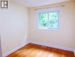 Bedroom featuring wood-finish flooring, white baseboards, and a bright window with a white frame - 