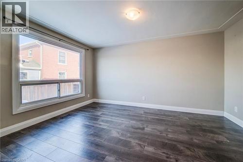 Spacious room featuring wood-finish flooring, a large multi-pane window, neutral wall paint, white trim, and a ceiling-mounted light fixture - 415-435 Garden Street Unit# 421, Cambridge, ON 