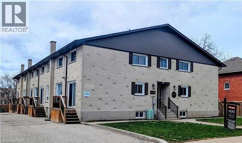 Multi-unit property featuring a light-colored brick exterior with dark trim and shutters, individual outdoor staircases, and a neatly maintained lawn area - 415-435 Garden Street Unit# 421, Cambridge, ON 