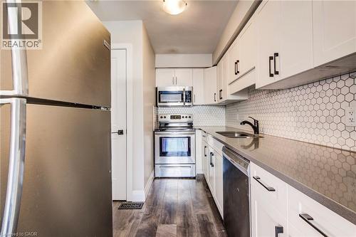Kitchen featuring white cabinetry with matte black hardware, stainless steel appliances, hexagon tile backsplash, dark countertops, and wood-finish flooring - 415-435 Garden Street Unit# 421, Cambridge, ON 