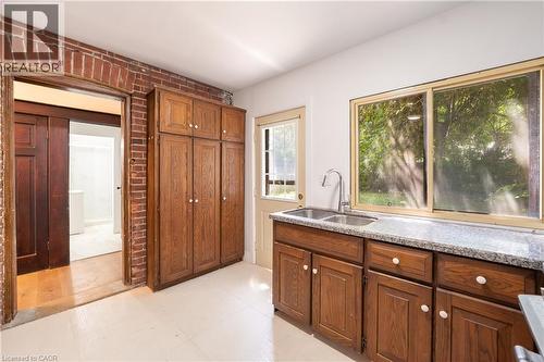 Kitchen featuring wood-finish cabinetry, a double basin sink with a gooseneck faucet, and stone countertops - 1274 Barton Street E, Hamilton, ON 