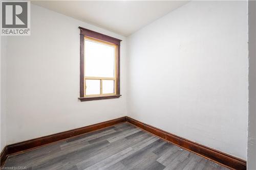 Room featuring a single window with dark wood trim, white walls, dark wood baseboards, and wood-finish flooring - 1274 Barton Street E, Hamilton, ON 