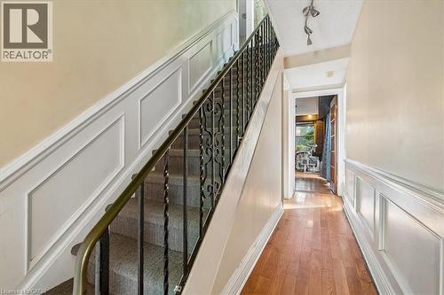 Carpeted staircase featuring an ornate wrought iron railing with a brass-finish handrail, complemented by wainscoting paneling - 80 Maclennan Avenue, Hamilton, ON 