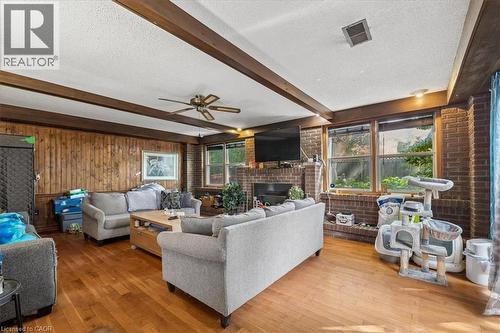 Spacious living area featuring wood-finish flooring, exposed ceiling beams, and a brick accent wall with a fireplace - 80 Maclennan Avenue, Hamilton, ON 