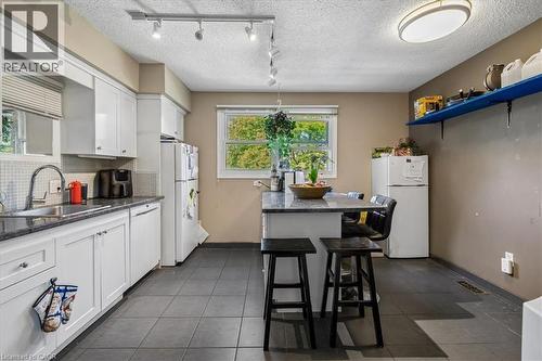 Kitchen featuring white cabinetry, dark countertop surfaces, a stainless steel sink with a gooseneck faucet, light-colored tile backsplash, and dark tile flooring - 80 Maclennan Avenue, Hamilton, ON 
