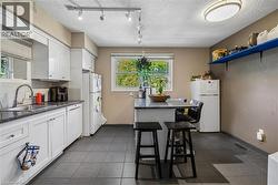Kitchen featuring white cabinetry, dark countertop surfaces, a stainless steel sink with a gooseneck faucet, light-colored tile backsplash, and dark tile flooring - 
