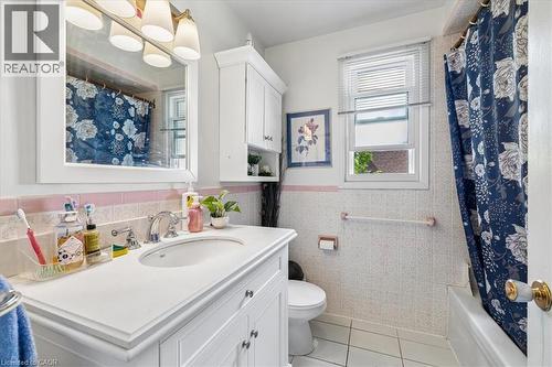 Bathroom featuring a white vanity with an integrated sink, built-in medicine cabinet, tiled walls with a pink accent stripe, and a window providing natural light - 80 Maclennan Avenue, Hamilton, ON 